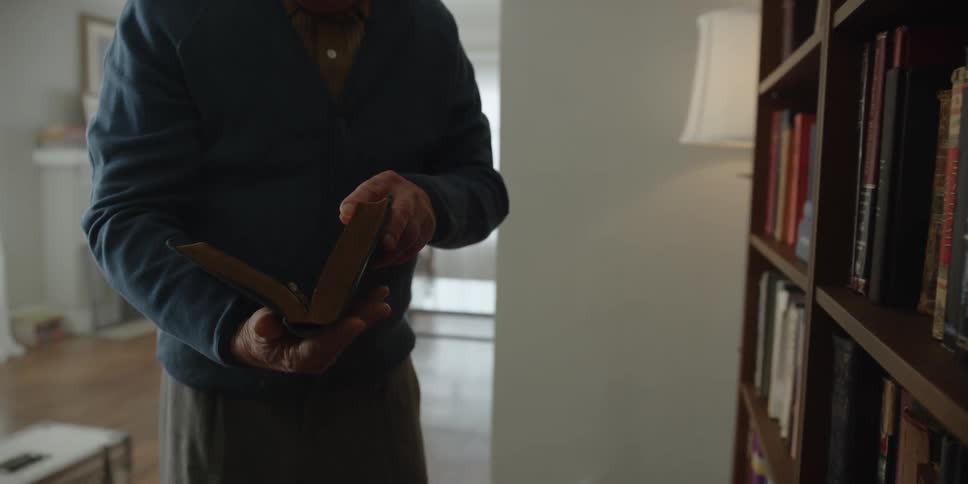 An elderly man removing a book from a bookshelf in a living room