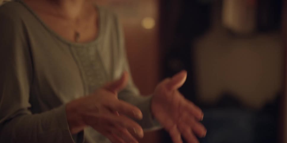 A woman is standing up talking and she holds out her hands as she speaks