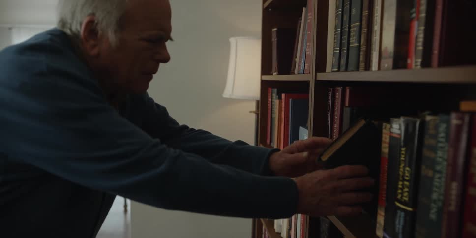 Elderly man takes book from bookshelves