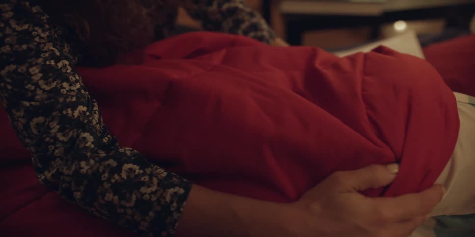 A mother covering her sleeping son with a red blanket