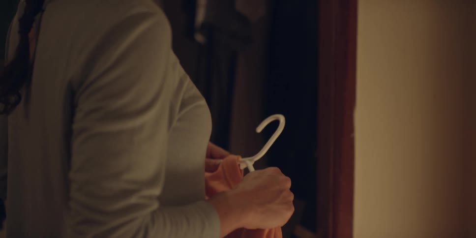 A young woman is putting clothes on a hanger in her closet