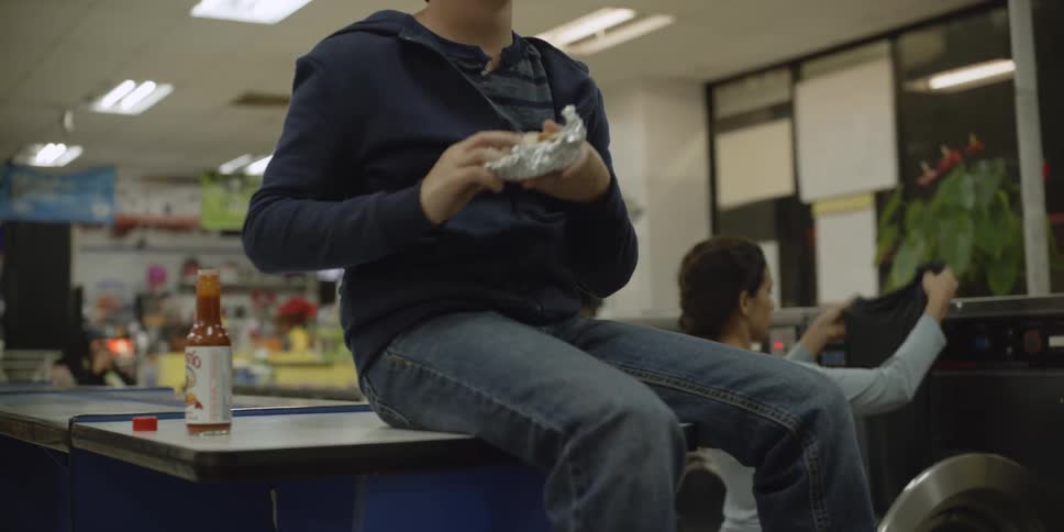 A child is eating while a woman does laundry