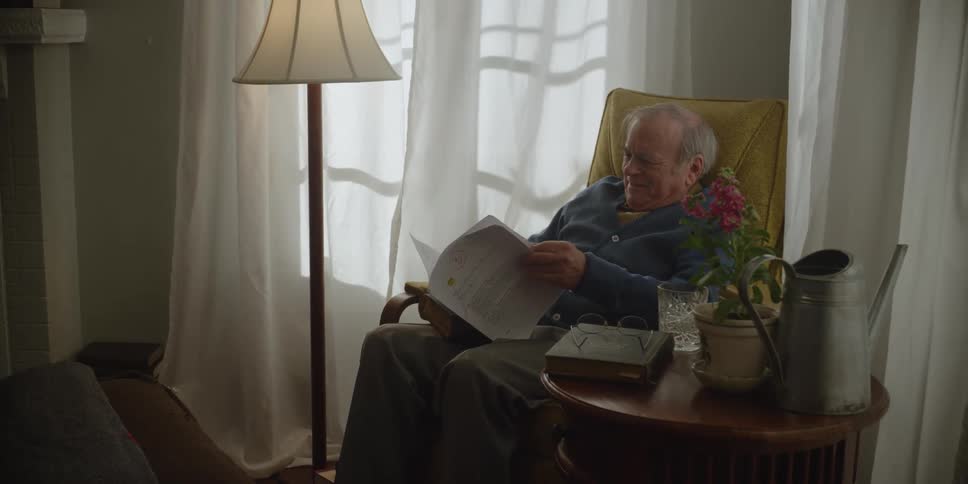 Elderly man sits in chair and smiles while reading papers