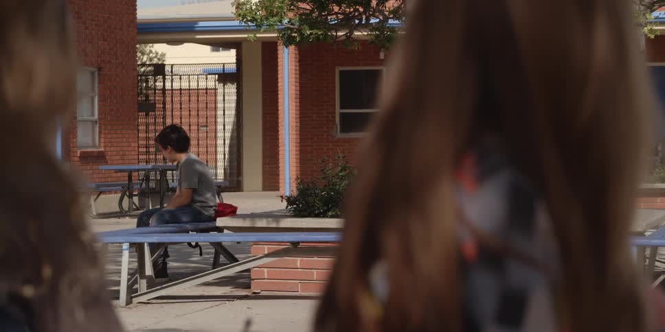 Two girls stare at a boy sitting on a bench in their apartment courtyard