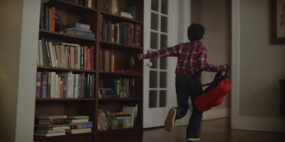 A young boy runs through a house as he takes his backpack off and drops it on the floor