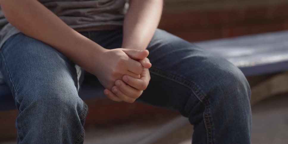 An adult is sitting down outside and holding there hands