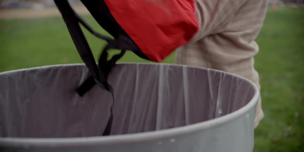 A boy grabs his backpack out of the trash