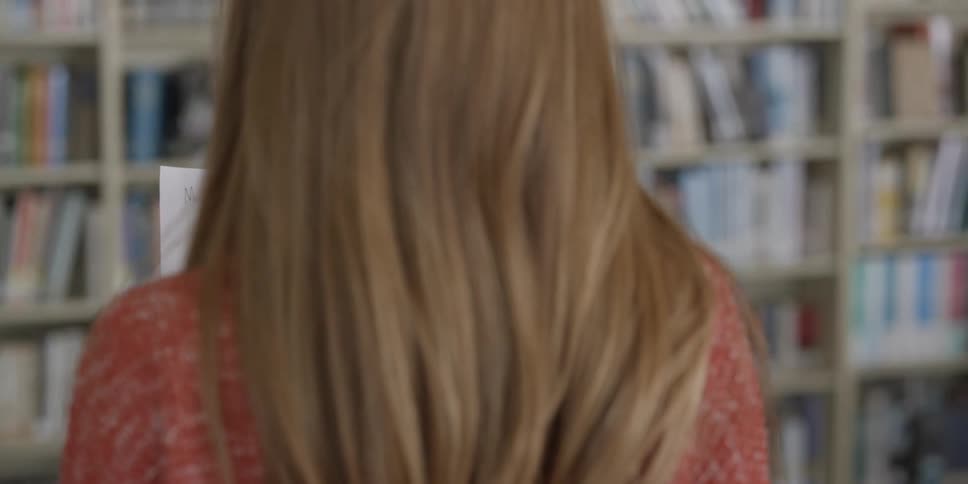 Back of a blonde girl reading a handwritten letter on a library at school