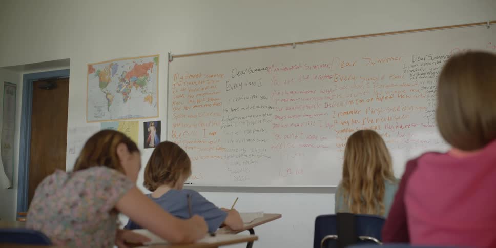 Students sit at desk writing in notebooks in the classroom