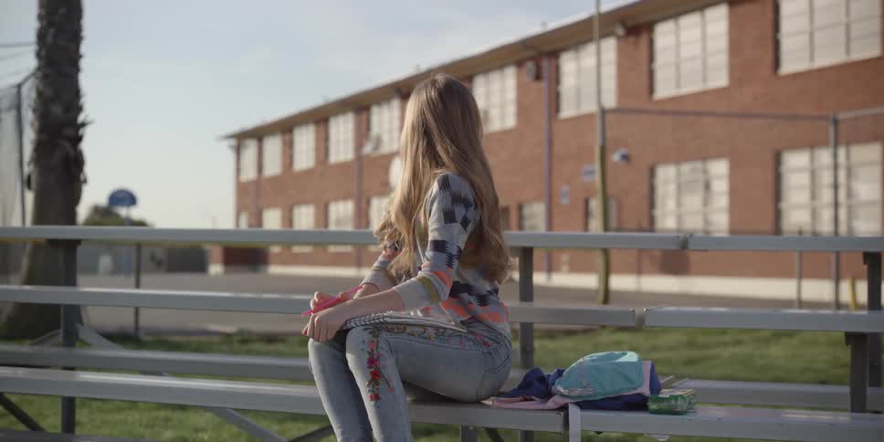 A young teenage girl is sitting outside of her school in the day time