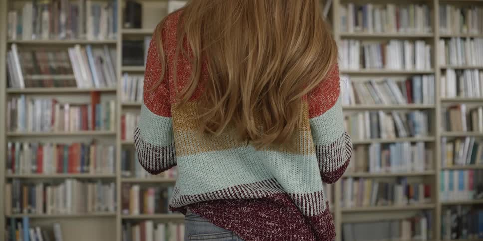 A woman stands still looking at a book in a library full of people