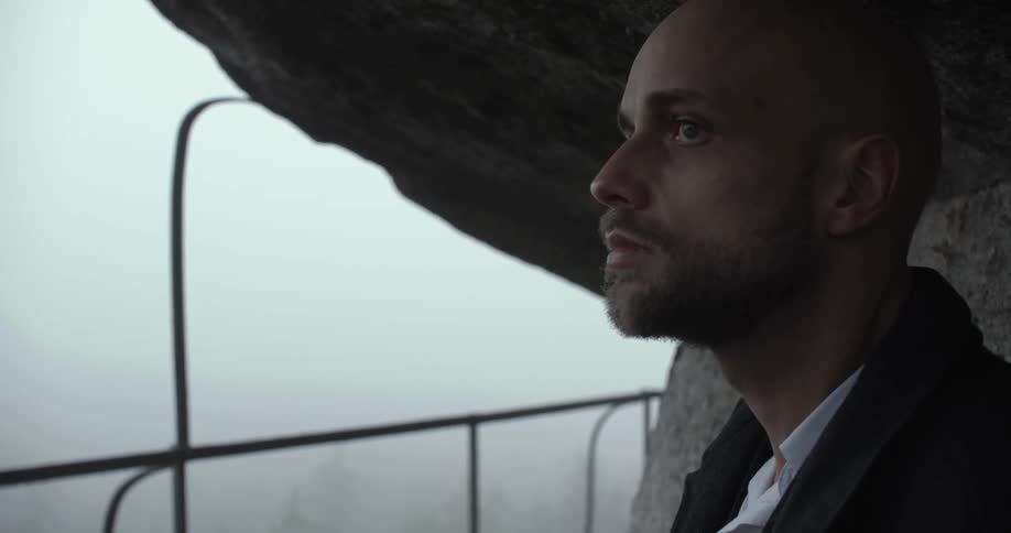 Man looking solemnly around from what appears to be a balcony on a very foggy day