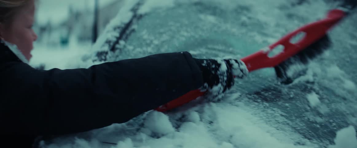 Girl uses an ice scraper to clean the windshield of a vehicle parked outdoors at winter