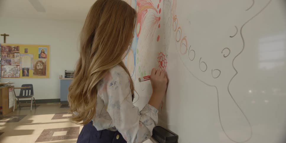 A young girl draws on a white board in a classroom