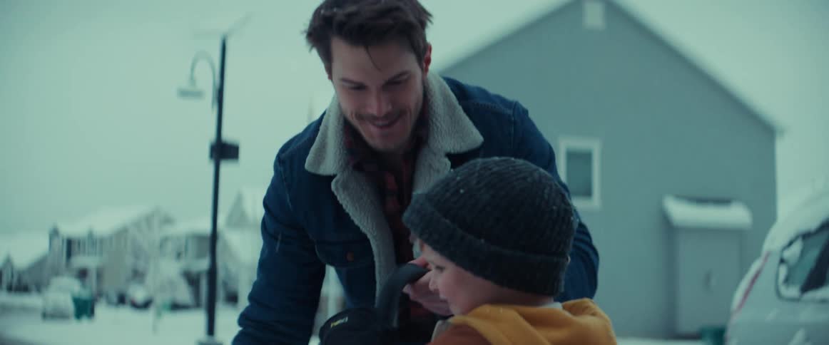 A man is outside in his driveway shoveling snow with his young son