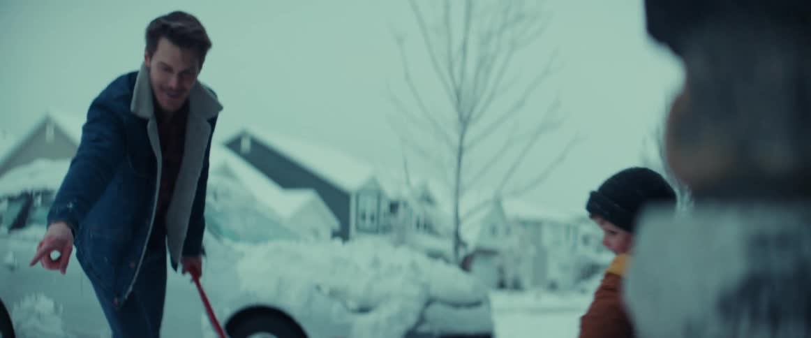 A child is carrying a shovel in the snow filled driveway
