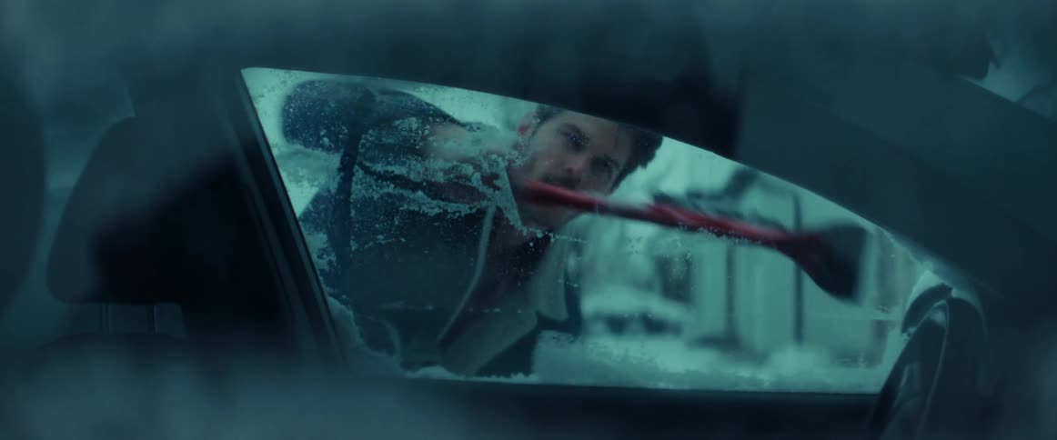 A man scrapes snow and ice off the driver side window of his car
