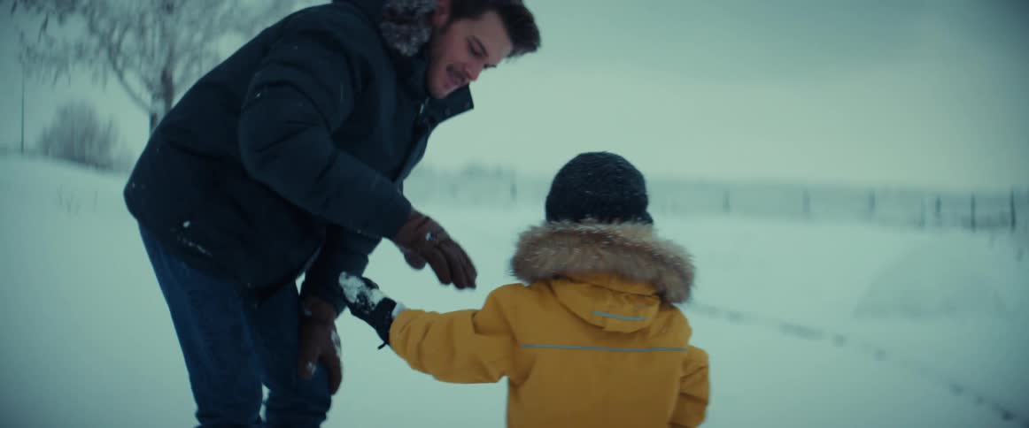 Man and young son hold hands walking near snow covered trees