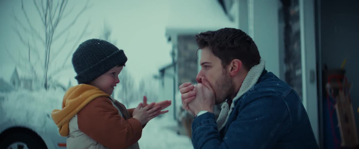 A man kneeling before a boy shows him how to warm his hands by rubbing them together and breathing on them on a winter day
