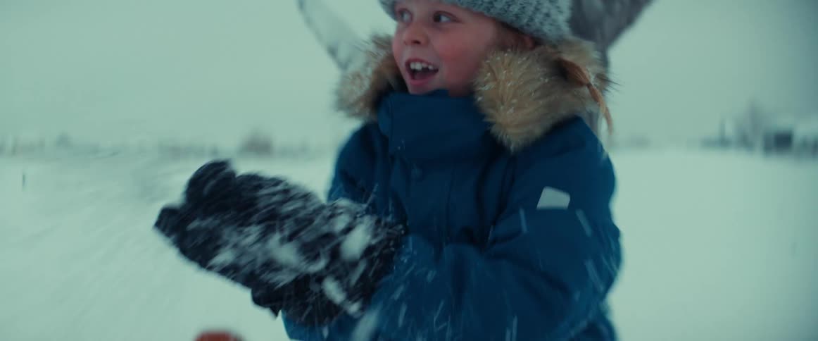 A young child throws snow outside while another child sits in the snow