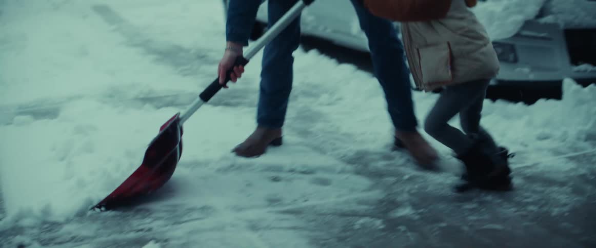 A little boy pushes a shovel with his father as he shovels a driveway