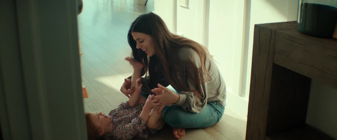A mother smiling and tickling her toddler while sitting on the floor