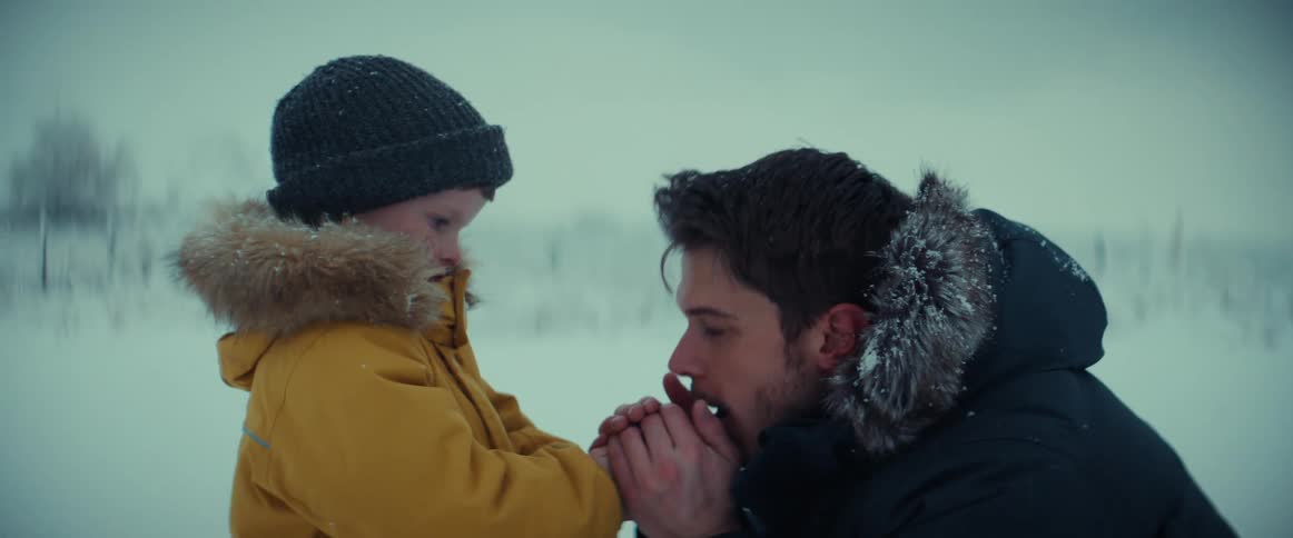 Man with boy in snow blowing hands to warm up
