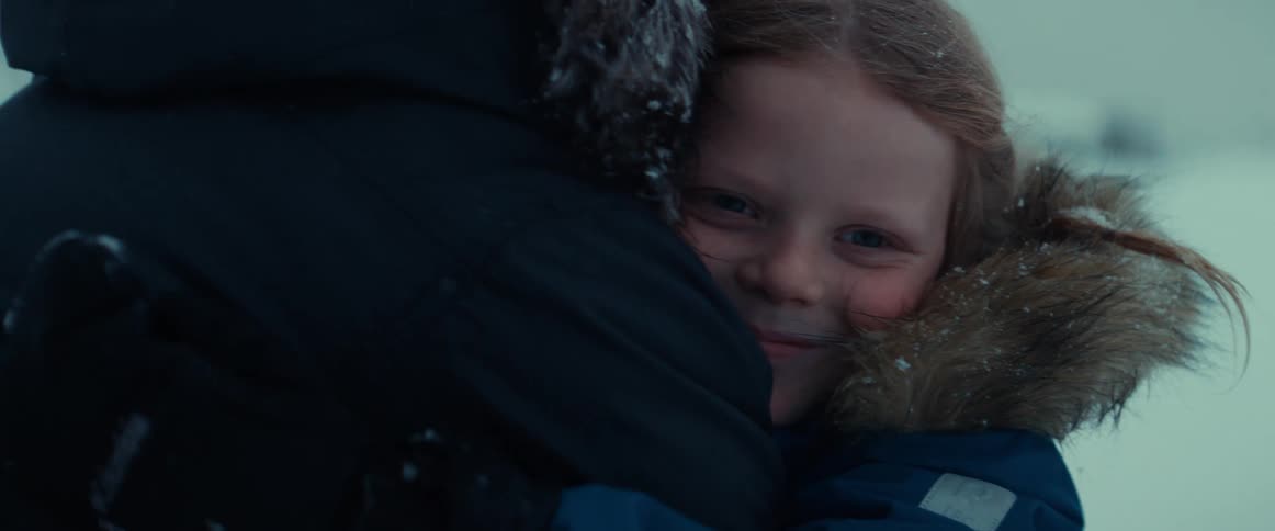 A young girl receiving a hug outside on a snowy winter day