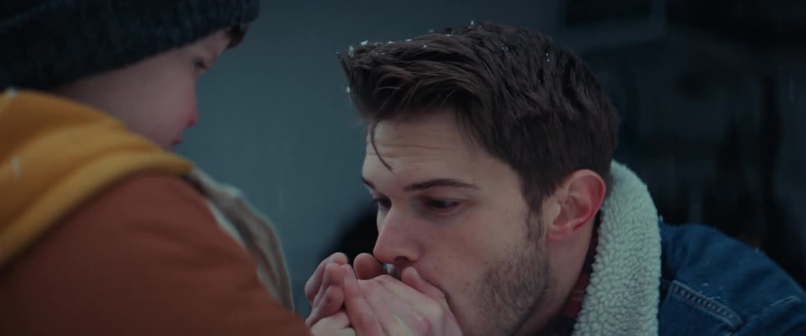 A man is outside on a cold winter day with his young son and rubbing his hands and blowing on them to warm them up