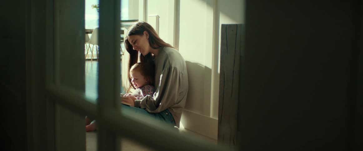 Mother holds daughter in her lap as they sit on floor reading