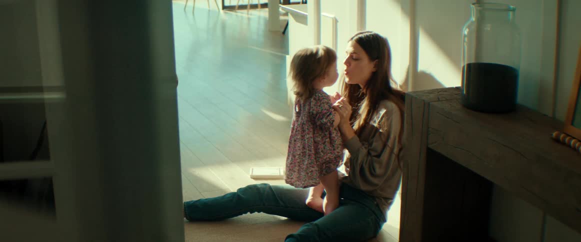 A mother kissing her baby girl while sitting on the floor