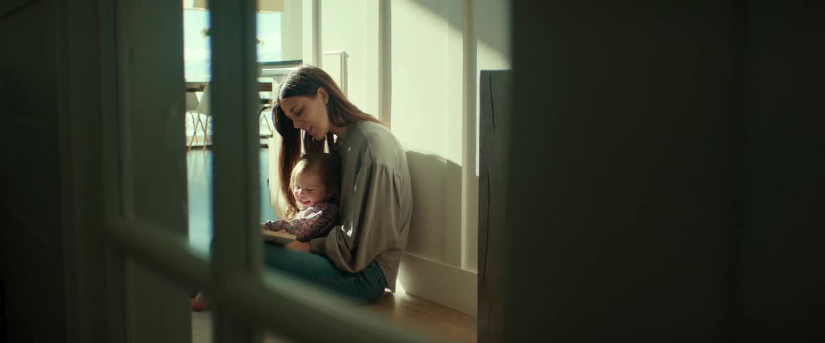 A woman is sitting in a hallway with her little girl in her lap as they look at a book together