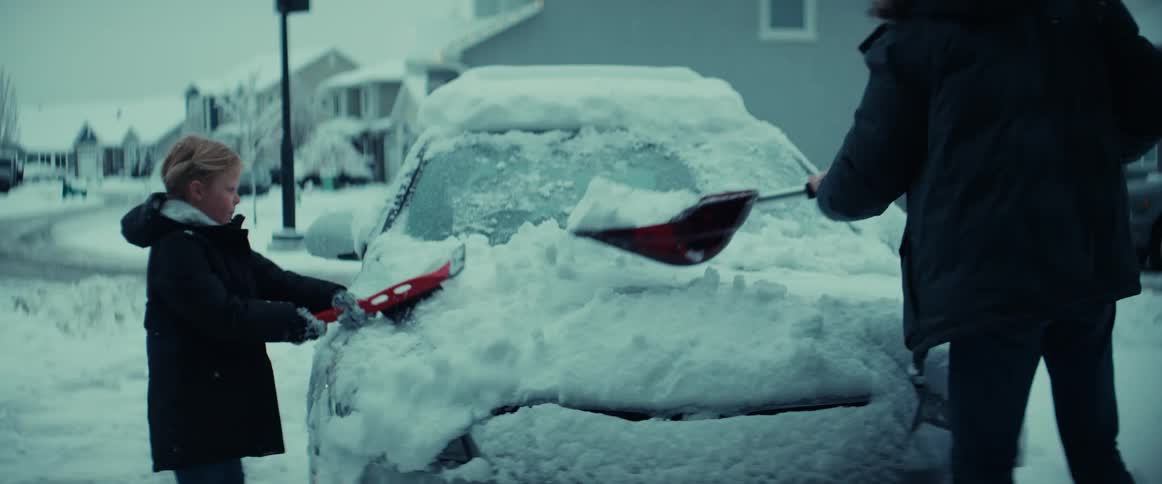 A father and daughter are cleaning snow off a car in a neighborhood