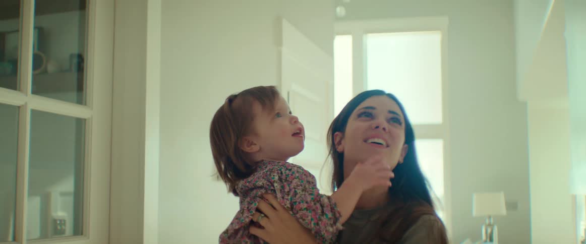 A woman is standing in a hallway playing with her little girl and holding her high in the hair