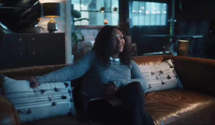 Woman sitting on couch in dim living room puts smartphone away and concentrates on television
