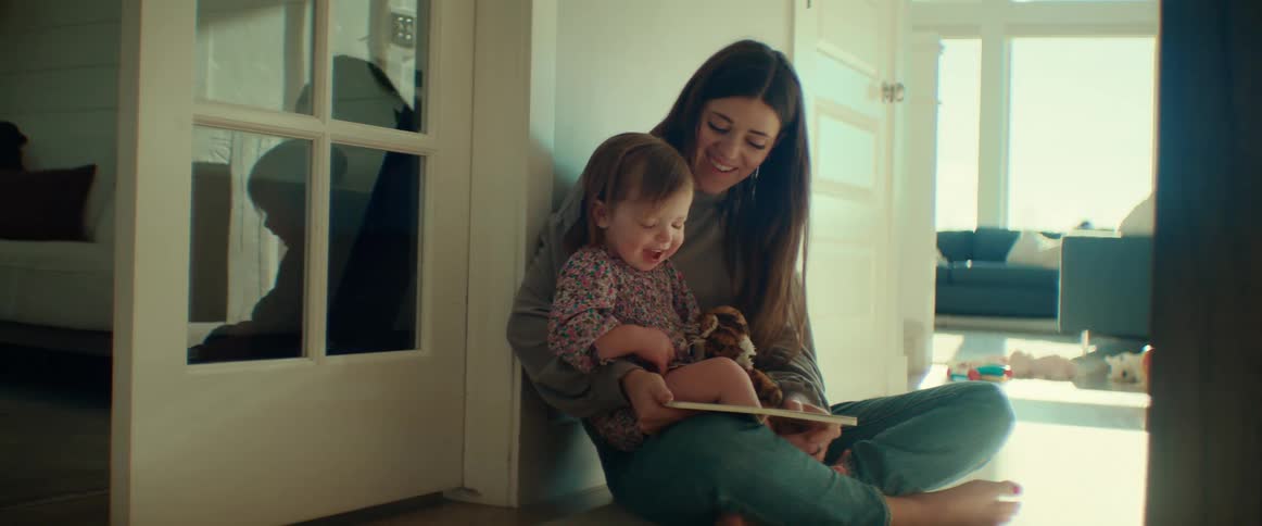 A woman is sitting in a hallway with her little girl in her lap as they look at a book together