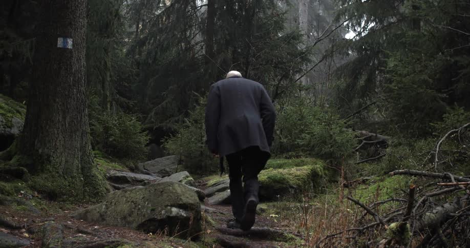 A man wearing a suit jacket hikes through the forest