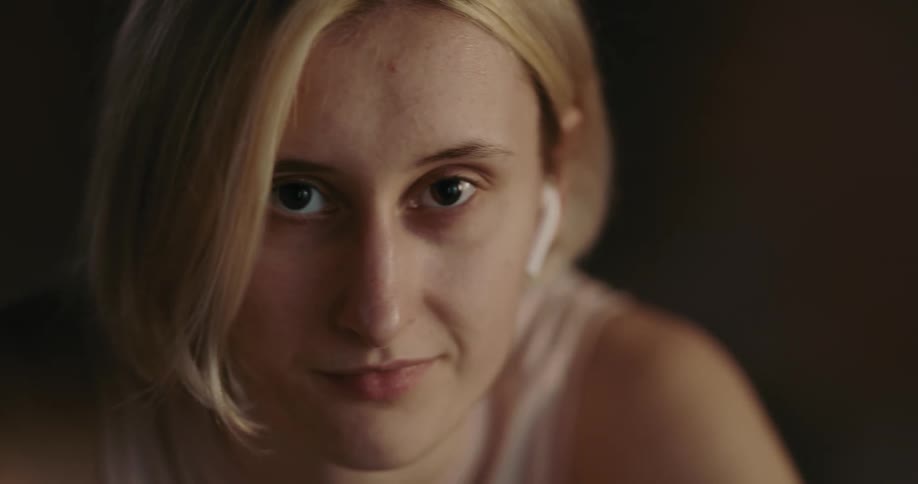Light shines on the face of a young woman with brown eyes and short blond hair as she rides an exercise bike