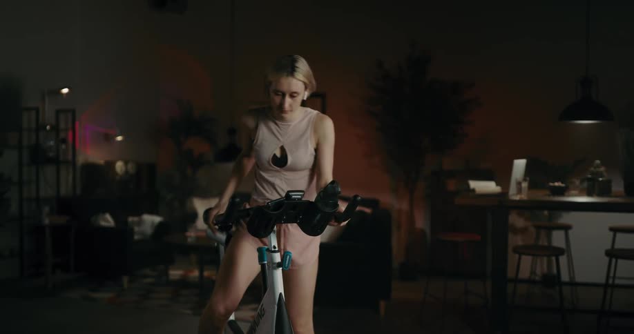 A woman puts earbuds in her ears before climbing onto a fitness bike and beginning to exercise