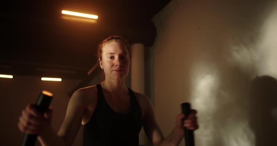 Woman with ponytail black tank top and shorts uses cross trainer in the gym