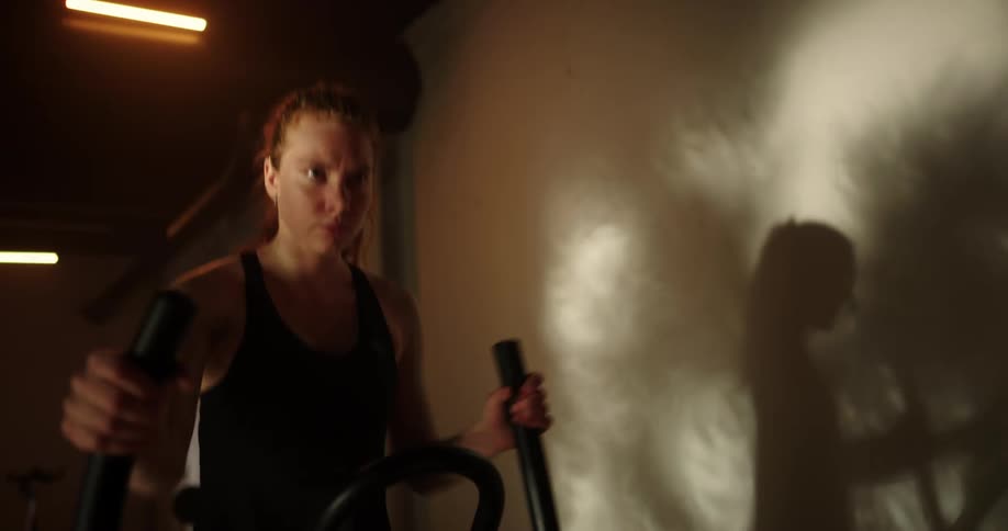 Woman with ponytail black top and shorts uses cross trainer at gym