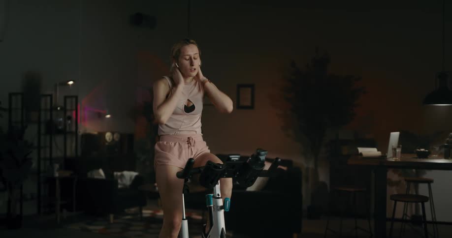 Blonde woman with bob pink shirt and shorts rides stationary bicycle
