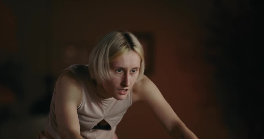 Determined blonde woman with bob pink shirt and shorts rides stationary bicycle