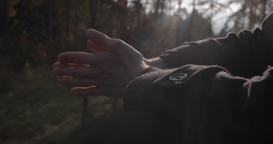 A man rubbing his palms together as he sits in a forest