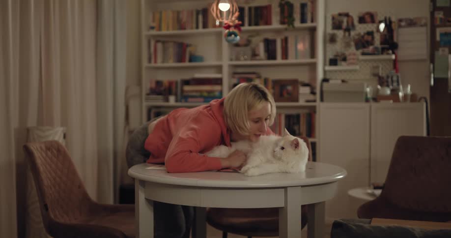 A woman leans down to kiss her cat while petting its fur