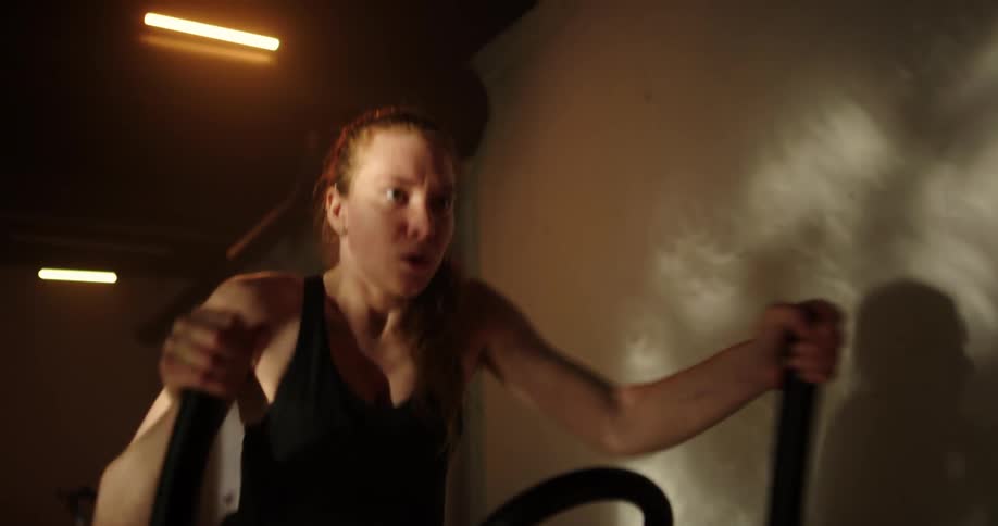 Determined woman with ponytail black top and shorts uses cross trainer at gym