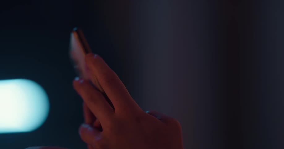 Woman texts on smartphone near blue light