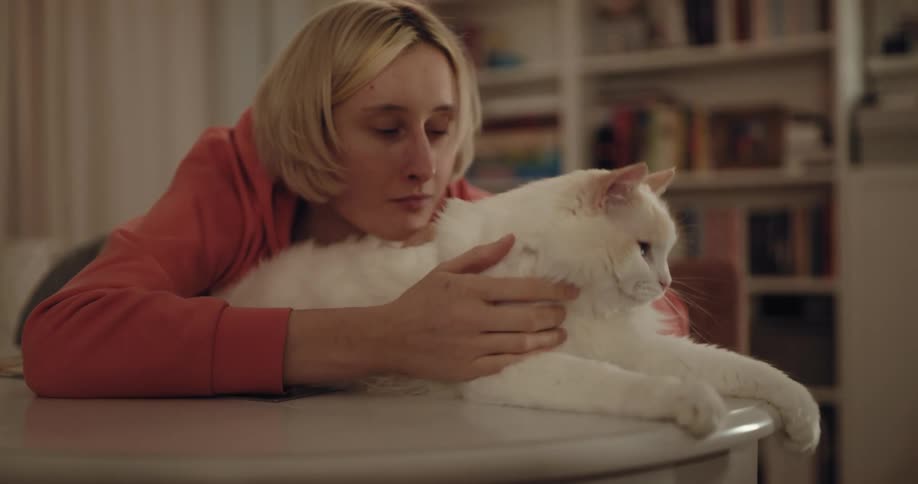 Blonde woman cuddles with white long haired cat as she pets it