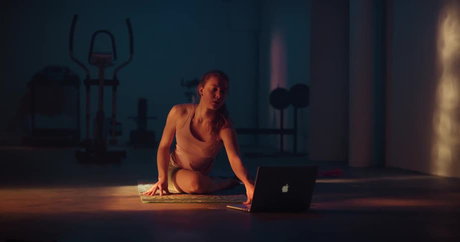 A woman doing yoga poses on a yoga mat in front of a laptop