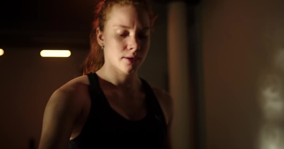 A woman is working out on an exercise machine as her shadow moves on the wall